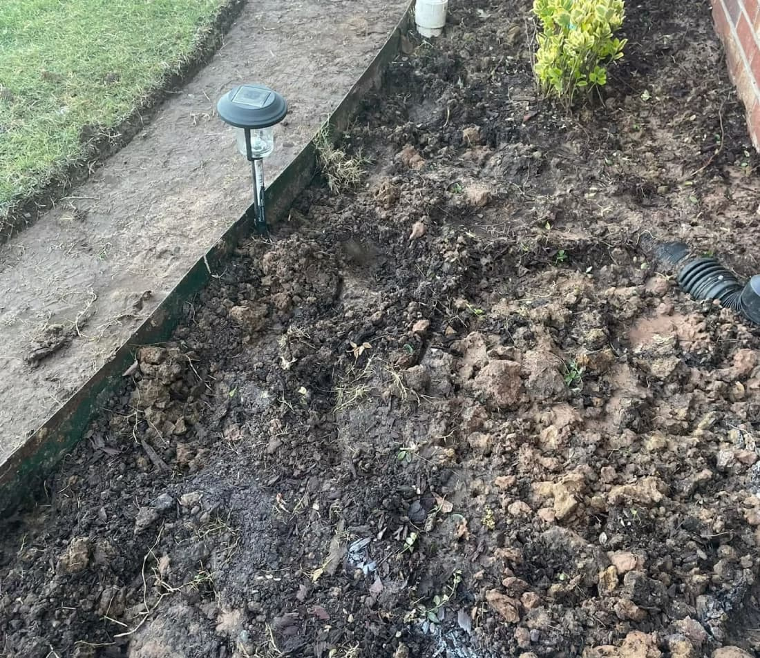 Compacted, cloddy heavy clay soil in a residential landscape bed next to lawn edging and a house foundation