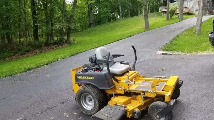 A yellow zero-turn lawn mower parked at the base of a steep, grassy hill, illustrating a landscape depression where cold air pools to create a frost pocket.