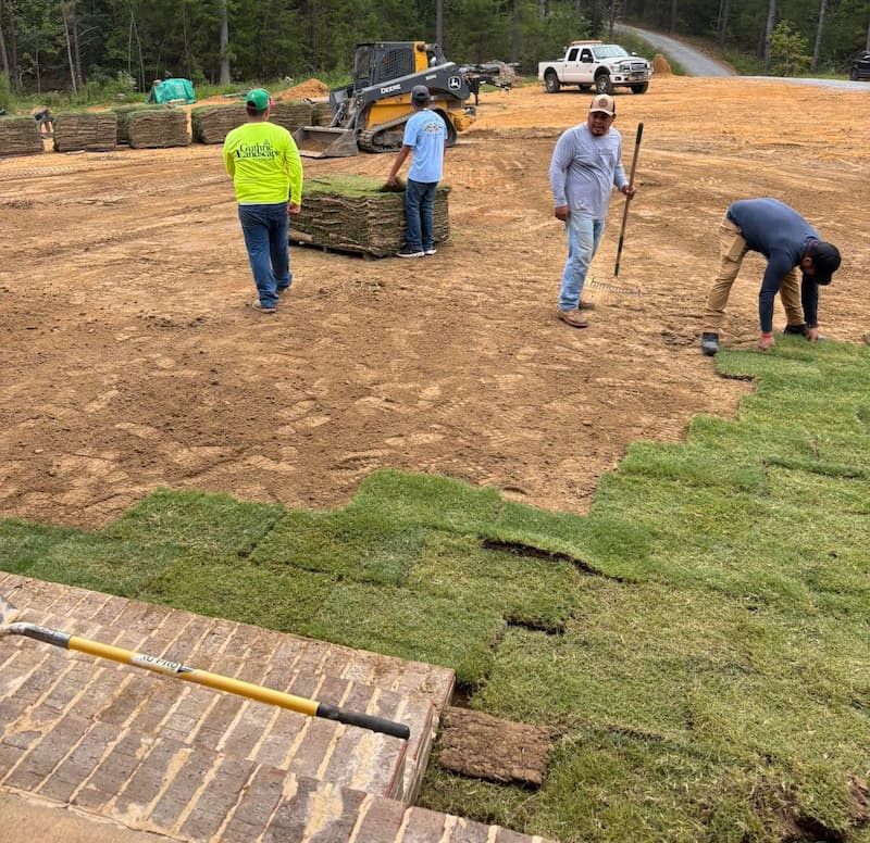 sod-installation-crew-laying-fresh-sod Landscaping crew installing pallets of fresh sod over bare soil during new lawn installation.