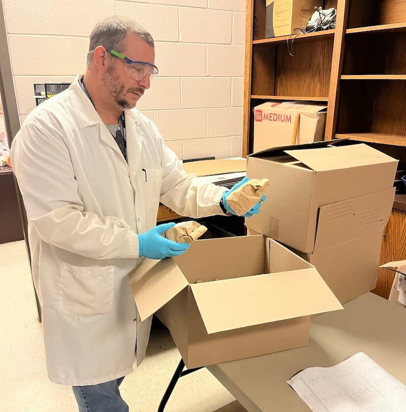 Dr. Gregory Olson in a lab coat and safety glasses unpacking sample bags at the LSU AgCenter Soil Testing and Plant Analysis Laboratory