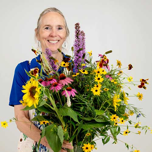 Lucy Bradley, NC State University Extension horticulture professor, holding a bouquet of coneflowers, black-eyed Susans, and wildflowers